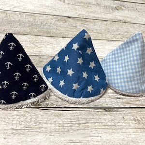 Könnte beinhalten: Drei Stoff-Babyspucktücher in Kegelform. Die Spucktücher sind aus blauem und weißem Stoff mit verschiedenen Mustern: Anker, Sterne und Gingham.