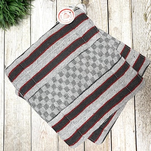 Könnte beinhalten: Zwei graue und rote gestreifte Küchentücher, die auf einer Holzoberfläche zusammengefaltet sind. Die Tücher haben ein kariertes Muster und sind aus einem weichen, saugfähigen Material gefertigt.