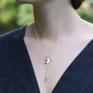 May include: A silver necklace with a detailed neuron pendant. The pendant is a realistic representation of a nerve cell with a central body and branching dendrites.