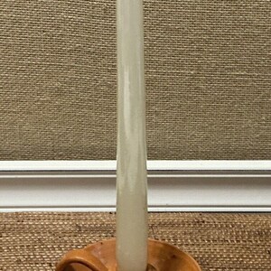 May include: A brown ceramic candle holder with a single white candle. The candle holder has a curved handle and a wide base.