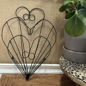 May include: A black wire heart-shaped frame with a decorative design. The frame is made of thin wire and has a delicate, intricate design.