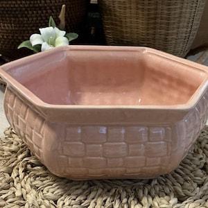 Puede incluir: Una maceta hexagonal de cerámica rosa con un patrón tejido. La maceta está vacía y lista para una planta.