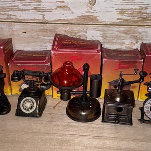 Puede incluir: Una colección de cinco réplicas en miniatura de aleación de zinc con acabado antiguo que incluye un reloj de cuco, un teléfono de disco, una linterna con pantalla roja, un molinillo de café y un reloj con números romanos, cada uno con su caja.