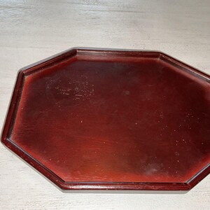 May include: A dark reddish-brown, octagonal wooden tray. The tray has a raised edge and a smooth, polished surface. The tray is empty and appears to be made of a solid piece of wood. The tray is likely used for serving or displaying items.
