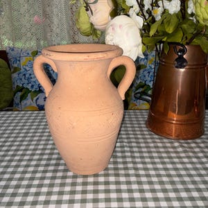 May include: A light tan terracotta vase with two side handles and a wide rim. The body of the vase features a subtle embossed geometric pattern consisting of repeating diamond shapes encircling the center, with a matte, earthy texture throughout.