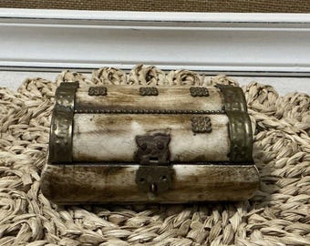 May include: A small, antique-looking wooden box with brass accents. The box has a hinged lid and a decorative latch. The box is sitting on a woven mat.