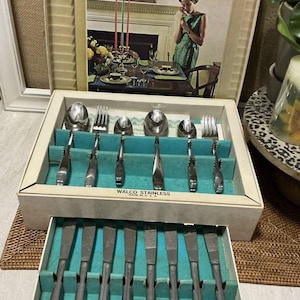 May include: A vintage set of stainless steel cutlery in a white box with a teal blue interior. The cutlery includes spoons, forks, and knives. The box has the text "Walco Stainless Made in U.S.A." printed on the front.