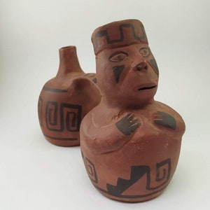 May include: Two terracotta pottery figures with black geometric designs. The figure on the right is a stylized human with a headdress and a face painted with black lines. The figure on the left is a rounder, more abstract shape.