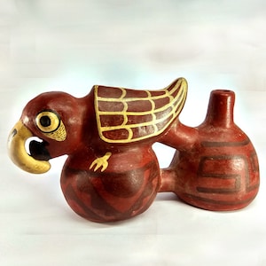May include: A red ceramic bird whistle with yellow and brown painted details. The bird has a large beak and a round body. The whistle has a small opening on the back for blowing.