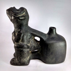 May include: Black ceramic sculpture of a stylised animal with a spout on its back. The animal has a rounded head and a long, slender body. The sculpture is decorated with a textured surface.