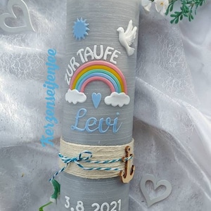 May include: Gray baptism candle with a rainbow, clouds, a dove, and a heart. The candle is decorated with a blue and white rope and a wooden anchor. The text "Zur Taufe Levi 3.8.2021" is written on the candle.  Variante Junge.