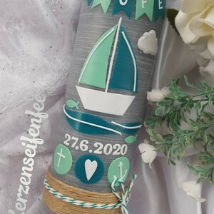 Könnte beinhalten: Graue Taufkerze mit einem weißen Segelboot, blauem Wasser und grün-weißen Flaggen, auf denen "Zur Taufe" steht. Die Kerze hat außerdem ein Kreuz, ein Herz und einen Anker, und das Datum "27.6.2020" und der Name "Luca" sind darauf geschrieben.