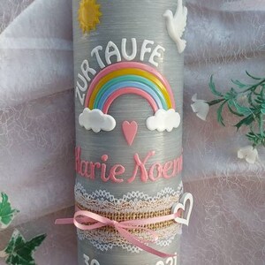 May include: Gray baptism candle with a white dove, a rainbow, and a pink heart. The candle is decorated with a white lace ribbon and a pink ribbon. The text "Zur Taufe Marie Noem 30.10.2021" is written on the candle.