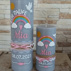 May include: Two gray pillar candles with a rainbow, clouds, and a heart design. The larger candle has the text "Zur Taufe Mia 08.07.2023" and the smaller candle has the text "Mia 08.07.2023".
