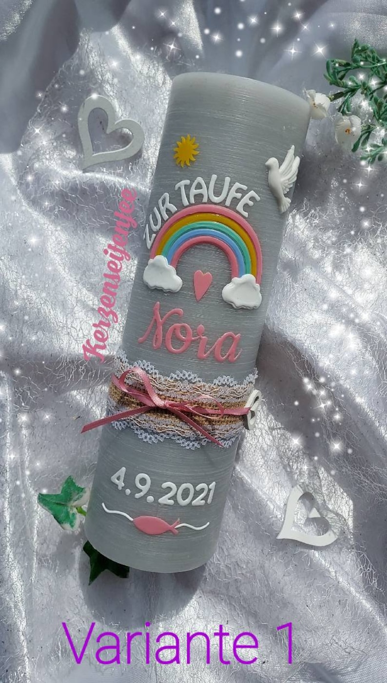 May include: Gray baptism candle with a rainbow, clouds, a heart, a dove, and a sun. The candle is decorated with a white lace ribbon and a pink bow. The text "Zur Taufe Nora 4.9.2021" is written on the candle.