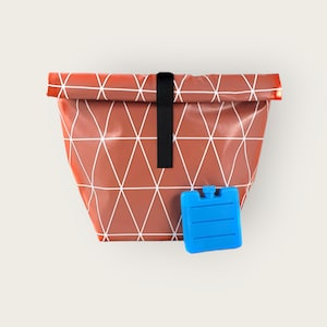 Könnte beinhalten: Eine braune Lunchtasche mit weißem geometrischen Muster und schwarzem Riemenverschluss. Ein kleiner blauer Kühlakku liegt neben der Tasche. Die Tasche ist so konzipiert, dass sie Lebensmittel kühl hält.