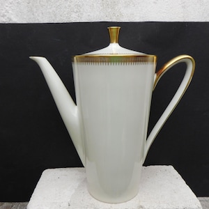 May include: A white porcelain coffee pot with a gold trim around the lid and handle. The pot has a classic design and is perfect for serving coffee.
