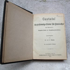 Op de afbeelding: Een vintage boek getiteld "Cantate! Mehrstimmige Lieder für Frauenchor" door C. und J. Enghlo. Het boek is gebonden in zwart en heeft een bruine omslag met de titel in zwart gedrukt.
