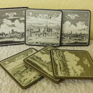 Pode incluir: Conjunto de cinco  tapetes quadrados com ilustrações em preto e branco de paisagens urbanas. Cada tapete tem uma borda preta e uma faixa branca com o nome da cidade e os anéis olímpicos. As cidades apresentadas são Munique, Kiel, Augsburgo e outras duas.