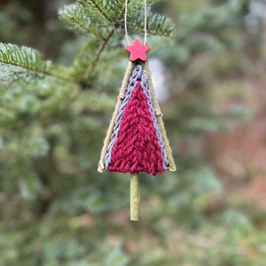 Puede incluir: Un adorno de árbol de Navidad de hilo rojo y gris con una estrella roja en la parte superior. El adorno está colgado de una rama.