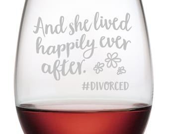 May include: A clear glass wine glass with the text "And she lived happily ever after. #DIVORCED" etched on the side. The glass is filled with red wine.