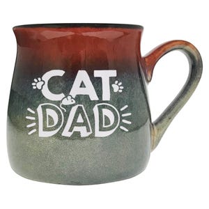 May include: A ceramic mug with a gradient finish, transitioning from red to green. The mug features the text "CAT DAD" in white, with paw prints and a mouse graphic. The handle is a light brown color.