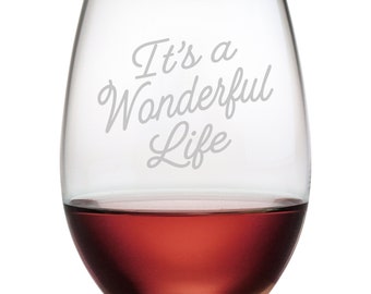 May include: A clear glass stemless wine glass with the text "It's a Wonderful Life" etched on the side. The glass is filled with red wine.