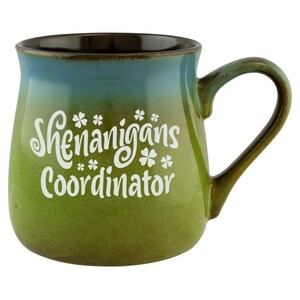 May include: A green and blue ceramic mug with a white design that says "Shenanigans Coordinator" with shamrock symbols.