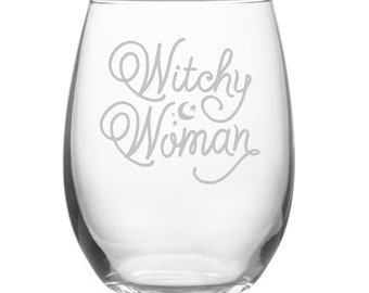 May include: A clear glass wine glass with the text "Witchy Woman" etched on the side. The text is in a cursive font with stars and crescent moons above the word "Woman".