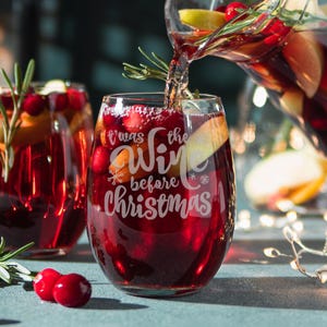 May include: Two clear wine glasses filled with red wine. The glass on the right has the text "It was the wine before Christmas" etched on the side.
