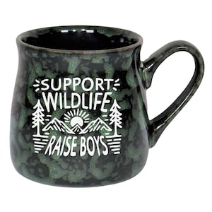 May include: A speckled green ceramic mug with a curved handle. The mug features white text that reads "SUPPORT WILDLIFE RAISE BOYS" with a graphic of a mountain range, trees, and a sun.