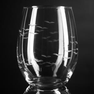 May include: A clear glass wine glass with a pattern of etched birds flying in formation. The glass has a wide base and a rounded bowl.