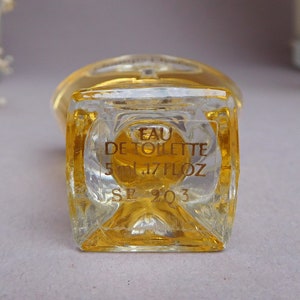 May include: A clear glass bottle of Eau de Toilette with a gold label. The label reads "Eau de Toilette 5 ml .17 fl oz SE 2Q3".