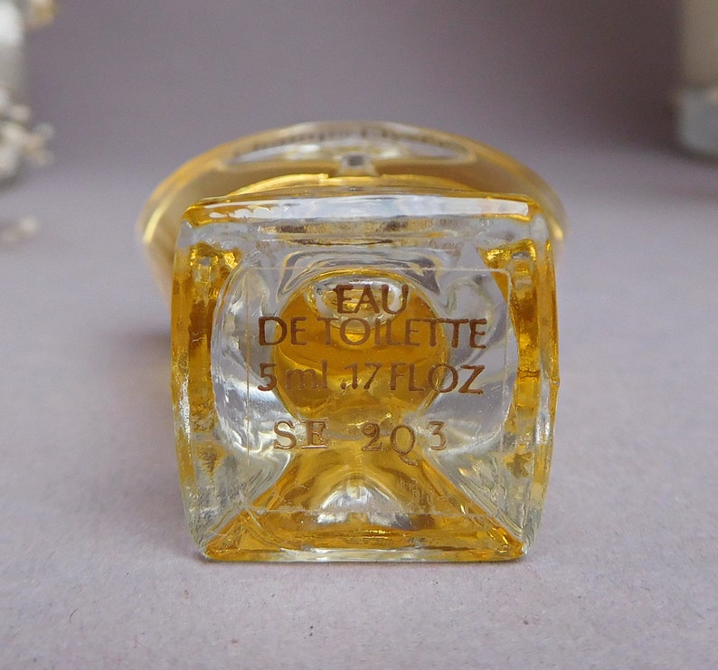 May include: A clear glass bottle of Eau de Toilette with a gold label. The label reads "Eau de Toilette 5 ml .17 fl oz SE 2Q3".