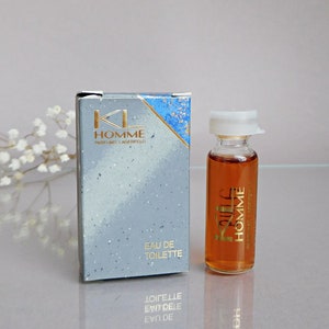 Peut inclure: Un échantillon de parfum "KL Homme" Eau de Toilette avec une boîte assortie. La boîte est bleu clair avec des lettres dorées et un motif éclaboussé. Le flacon de parfum est transparent avec un bouchon blanc et des lettres dorées.