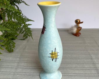 Op de afbeelding: Een lichtblauwe keramische vaas met een gele binnenkant. De vaas heeft een afgeronde body en een uitlopende bovenkant. Het heeft rode en gele kruisarcering ontwerpen. De vaas is ongeveer 18 cm hoog.