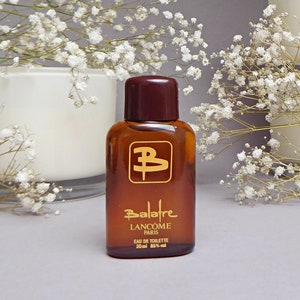 Könnte beinhalten: Eine braune Glasflasche von Lancôme Balafre Eau de Toilette. Die Flasche hat einen dunkelbraunen Deckel und goldfarbene Schrift. Das Etikett enthält den Markennamen, den Duftnamen und das Volumen: 20 ml.