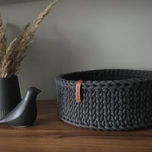 Una cesta decorativa tejida, un recipiente para guardar objetos pequeños, un elemento decorativo en un estante de una habitación o baño. Graphite