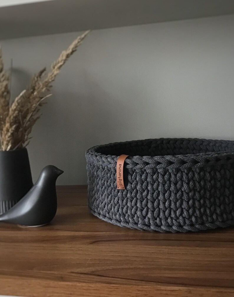 Una cesta decorativa tejida, un recipiente para guardar objetos pequeños, un elemento decorativo en un estante de una habitación o baño. Graphite
