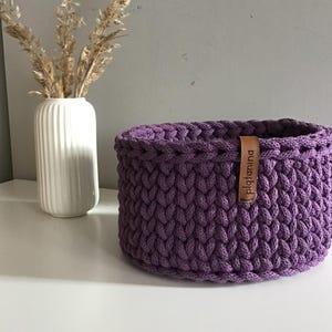 Una cesta decorativa tejida, un recipiente para guardar objetos pequeños, un elemento decorativo en un estante de una habitación o baño. Violet