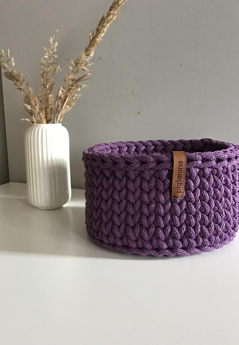 Una cesta decorativa tejida, un recipiente para guardar objetos pequeños, un elemento decorativo en un estante de una habitación o baño. Violet