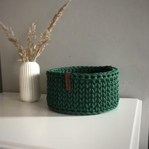 Una cesta decorativa tejida, un recipiente para guardar objetos pequeños, un elemento decorativo en un estante de una habitación o baño. Pine green