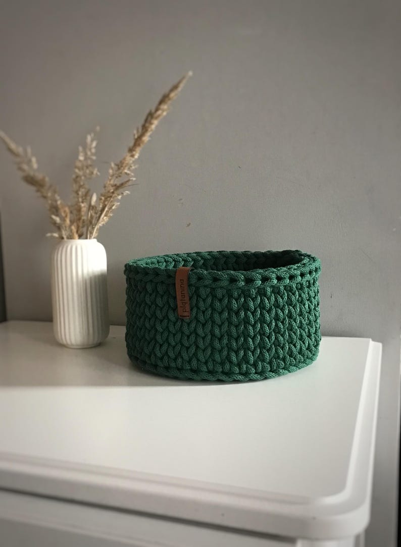 Una cesta decorativa tejida, un recipiente para guardar objetos pequeños, un elemento decorativo en un estante de una habitación o baño. Pine green