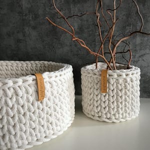 Una cesta decorativa tejida, un recipiente para guardar objetos pequeños, un elemento decorativo en un estante de una habitación o baño. Off white