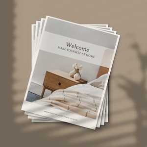 May include: A stack of brochures with a white background and the text "Welcome Make Yourself at Home". The brochure features a photo of a wooden nightstand with a drawer and a white ceramic vase with white flowers on top. A white and beige striped bedspread is visible in the background.