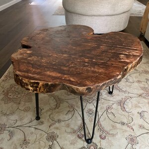 May include: A rustic wooden coffee table with a live edge top and black hairpin legs. The table is sitting on a patterned rug.
