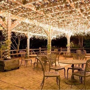 May include: A patio with a wooden pergola covered in white string lights. The patio is furnished with brown metal chairs and tables.