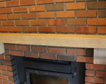 May include: A wooden mantel shelf with a light brown stain, mounted above a black fireplace with a brick surround.