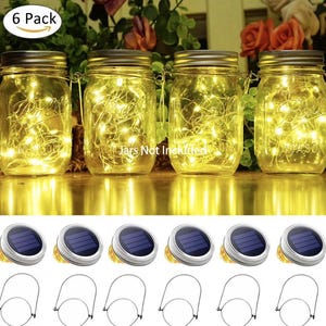 May include: A set of six solar-powered mason jar lid lights with warm white LED string lights. The image shows the jars lit up, along with the solar panels and handles. The jars are not included.