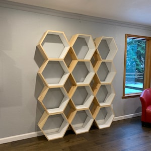 May include: A wooden hexagonal shelf unit with white painted shelves. The shelf unit is made of natural wood and has a modern design.